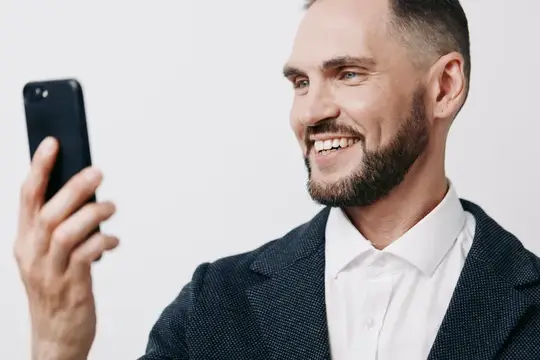 Улыбающийся бородатый мужчина в пиджаке смотрит в смартфон