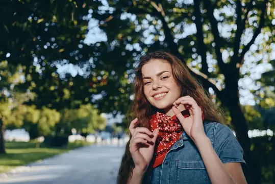 Улыбающаяся девушка с красным платком на шее в летнем парке