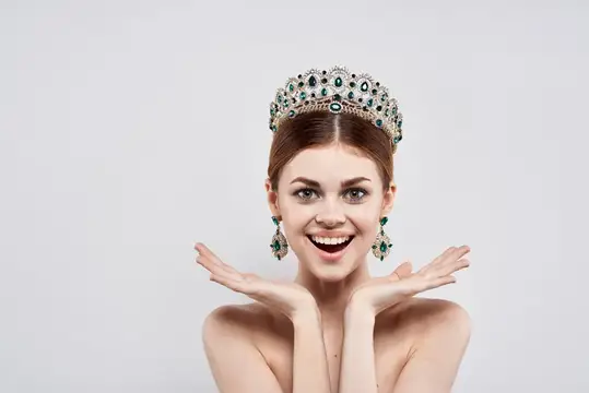 Улыбающаяся девушка в короне с изумрудами на сером фоне
