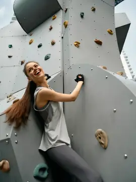 Бодрая молодая женщина в спортивной одежде карабкается по современной скалодромической стене, энергично улыбаясь