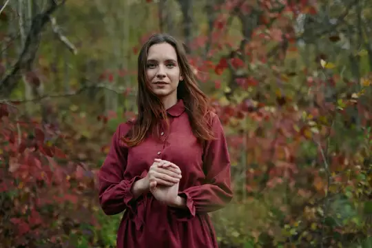Молодая женщина в бордовом платье стоит в осеннем лесу