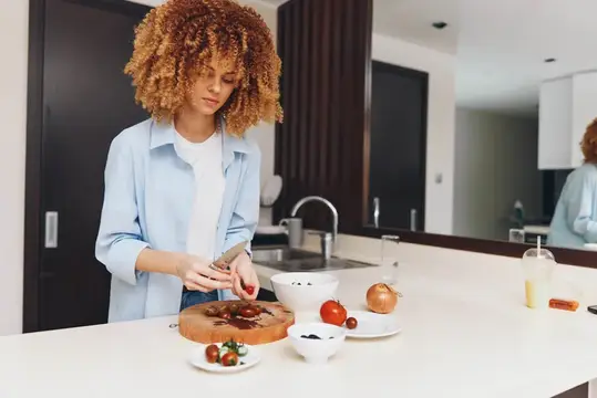 Кудрявая девушка режет овощи на современной светлой кухне