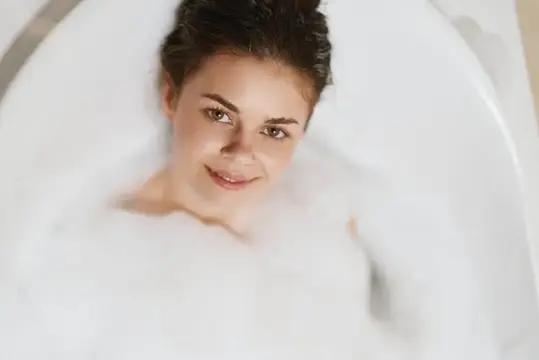 Молодая женщина с темными волосами улыбается, лежа в пенной ванне