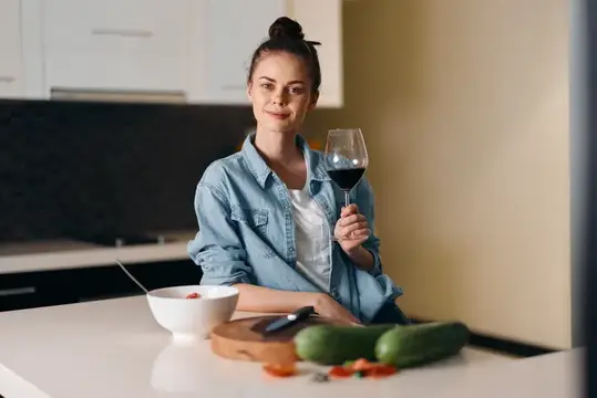Молодая женщина с бокалом красного вина на кухне