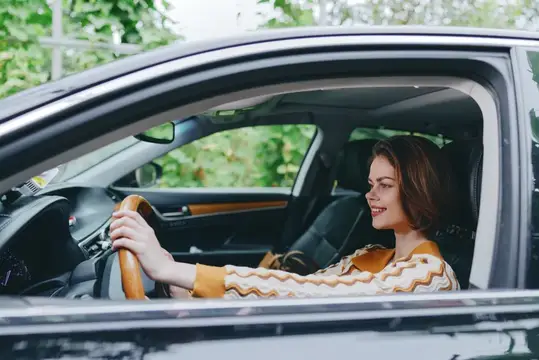 Улыбающаяся темноволосая женщина за рулём автомобиля