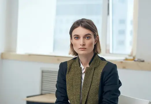 Светловолосая женщина в строгом пиджаке у окна в офисе