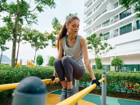 Спортивная девушка выполняет подъем коленей на уличных брусьях