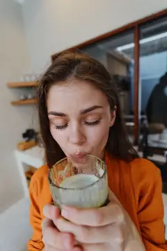 Молодая женщина в оранжевом свитере пьёт зелёный смузи из стакана