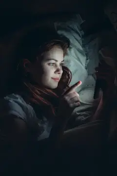 Молодая женщина лежит в темноте и смотрит на экран смартфона