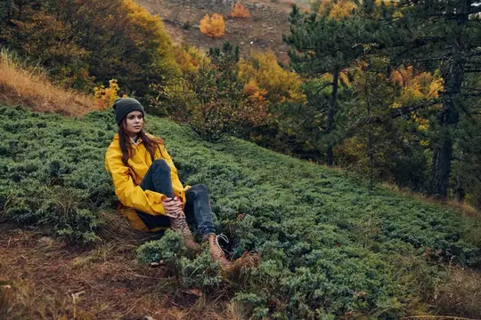 Осенний пейзаж: женщина в жёлтом дождевике сидит на обочине холма, окружённая разноцветной листвой