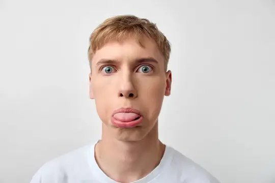 Молодой блондин с высунутым языком и выпученными глазами на белом фоне