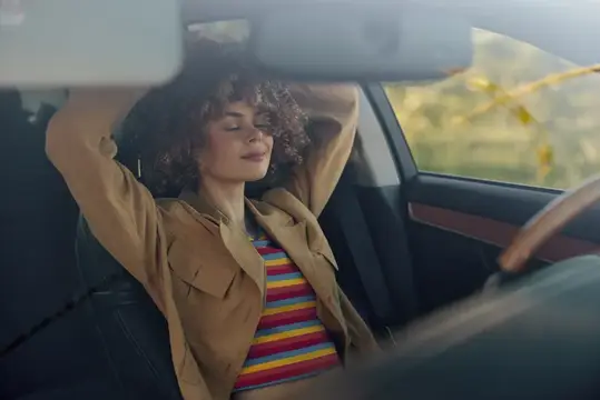 Кудрявая девушка с закрытыми глазами отдыхает в салоне автомобиля