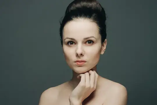 Молодая женщина с темными волосами смотрит прямо на сером фоне