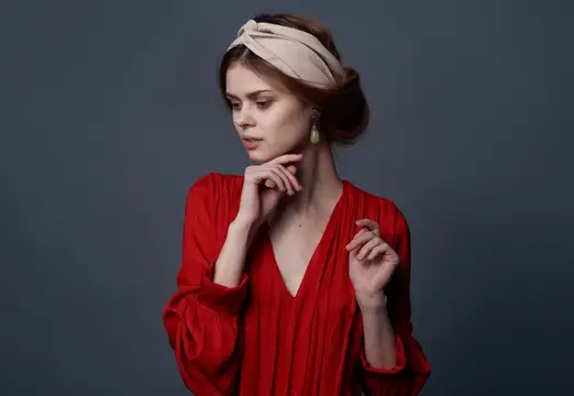 Задумчивая молодая женщина в красном платье на сером фоне