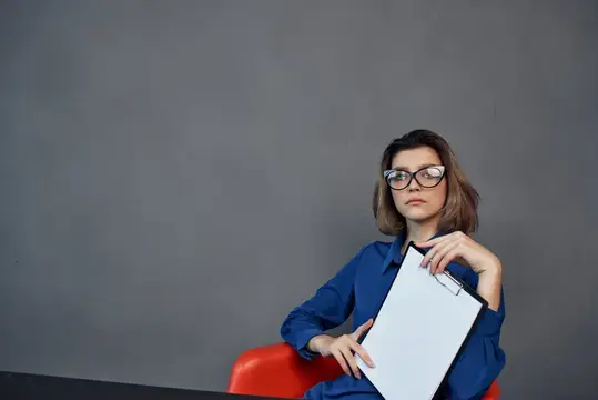 Девушка в очках с планшетом сидит на красном стуле