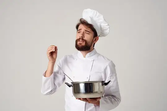 Задумчивый бородатый повар с кастрюлей пробует блюдо на вкус