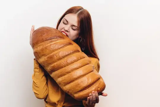 Эмоциональная женщина широко открывает рот, голод, буханка хлеба, мучное изделие