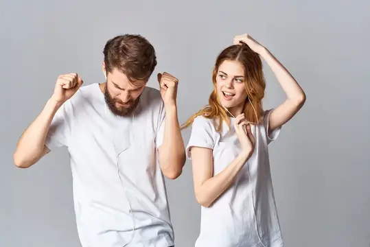 Молодые мужчина и женщина в белых футболках танцуют в наушниках