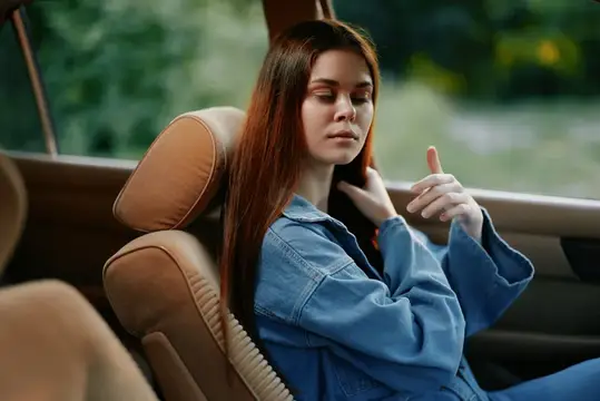 Рыжеволосая девушка в джинсовой куртке отдыхает на заднем сиденье автомобиля