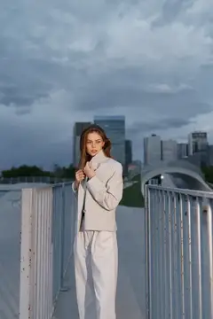 Молодая женщина в светлом костюме стоит на мосту на фоне города