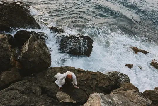 Женщина в белом платье лежит на скалах у бурного моря
