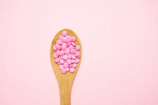 Розовые круглые драже на деревянной ложке на розовом фоне