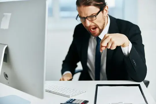 Разъяренный мужчина в очках кричит на монитор в офисе