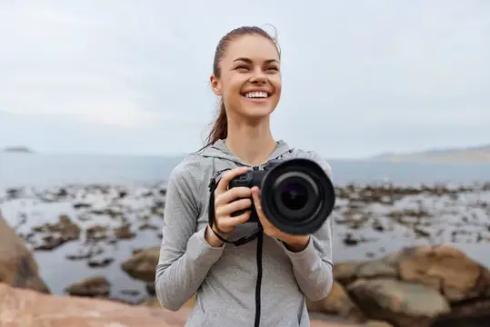 Улыбающаяся девушка с фотокамерой на берегу моря