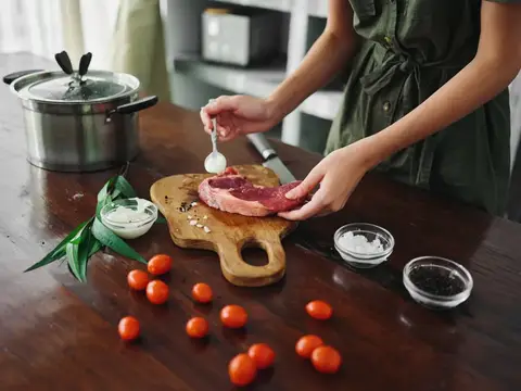 Женщина солит стейк на деревянной доске на кухне