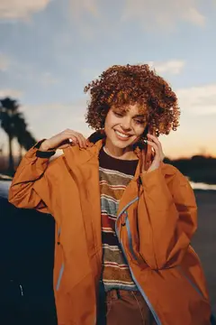 Рыжеволосая девушка в оранжевой куртке улыбается на закате