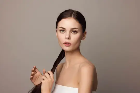 Молодая женщина с длинной темной косой на сером фоне