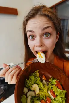 Удивлённая девушка ест яйцо с салатом из миски