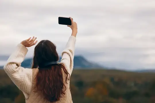 Девушка в свитере фотографирует пейзаж на телефон