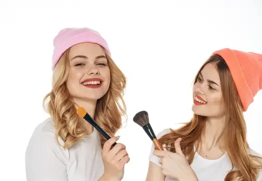 Две улыбающиеся девушки в шапках с кистями для макияжа