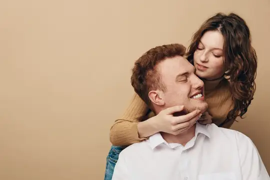 Девушка обнимает улыбающегося парня с закрытыми глазами на бежевом фоне