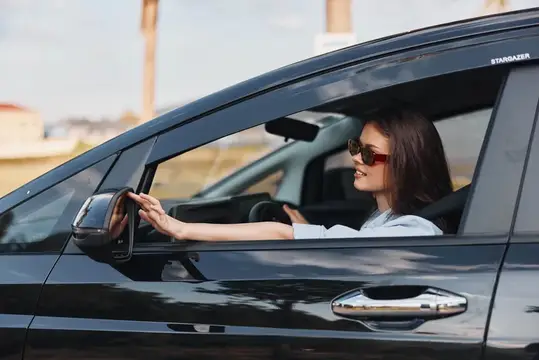 Женщина на водительском сиденье автомобиля, положив руку на руль, задумчиво смотрит в окно, запечатлевая момент размышлений и путешествия