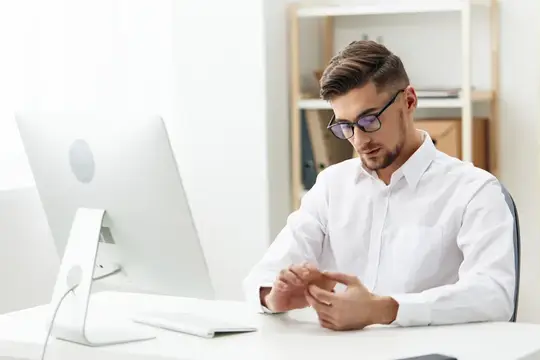 Молодой мужчина в очках и белой рубашке работает за компьютером в офисе