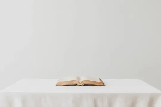 Раскрытая книга с золотистым обрезом лежит на белой скатерти