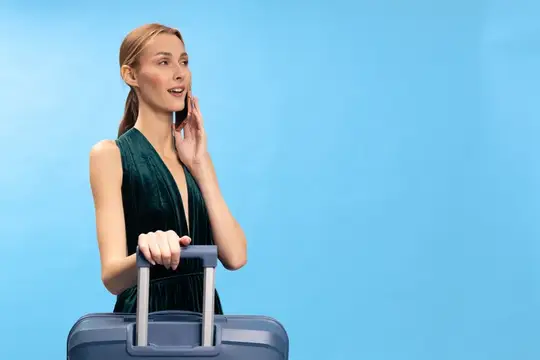 Улыбающаяся женщина с чемоданом говорит по телефону на голубом фоне
