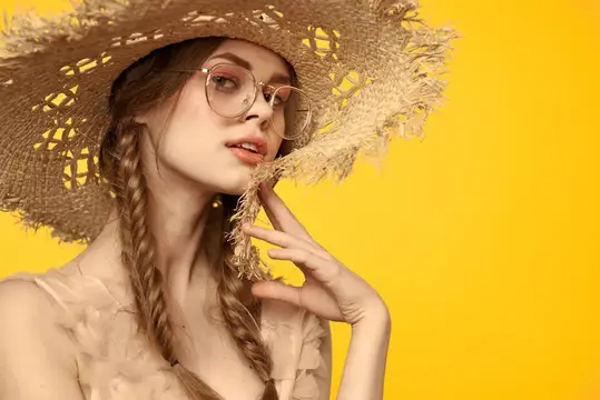 Молодая девушка в соломенной шляпе и очках на жёлтом фоне