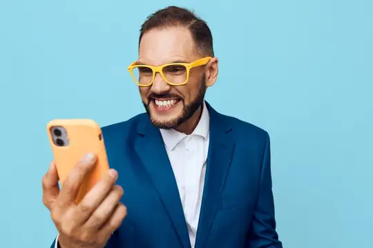 Улыбающийся бородатый мужчина в жёлтых очках смотрит в телефон