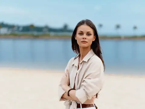 Молодая темноволосая женщина стоит на песчаном берегу у воды