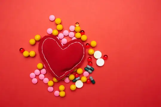 Красное сердце с белой строчкой в окружении разноцветных конфет на красном фоне