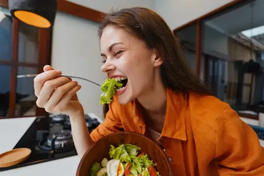 Молодая женщина с аппетитом ест салат из миски на кухне
