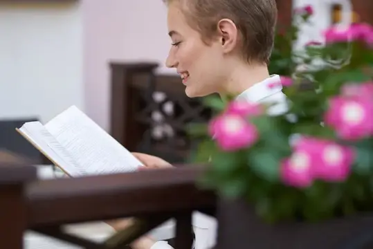 Улыбающаяся девушка с короткой стрижкой читает книгу у окна