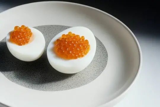Крупный план изысканных яиц пашот, украшенных яркой оранжевой икрой, подчёркивающий изысканную подачу блюда и кулинарное мастерство в минималистичной обстановке