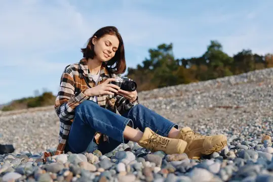 Непринуждённый портрет женщины-фотографа на открытом воздухе на каменистом берегу