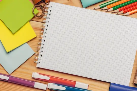 Открытый блокнот в клетку с цветными ручками и стикерами на деревянном столе