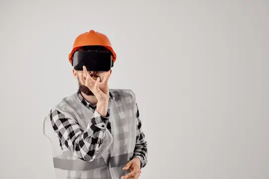 Строитель в оранжевой каске и VR-очках на сером фоне