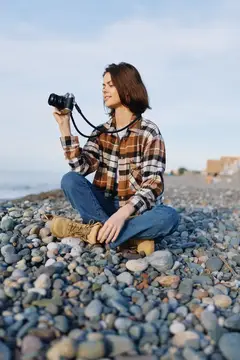 Девушка с фотокамерой сидит на каменистом берегу